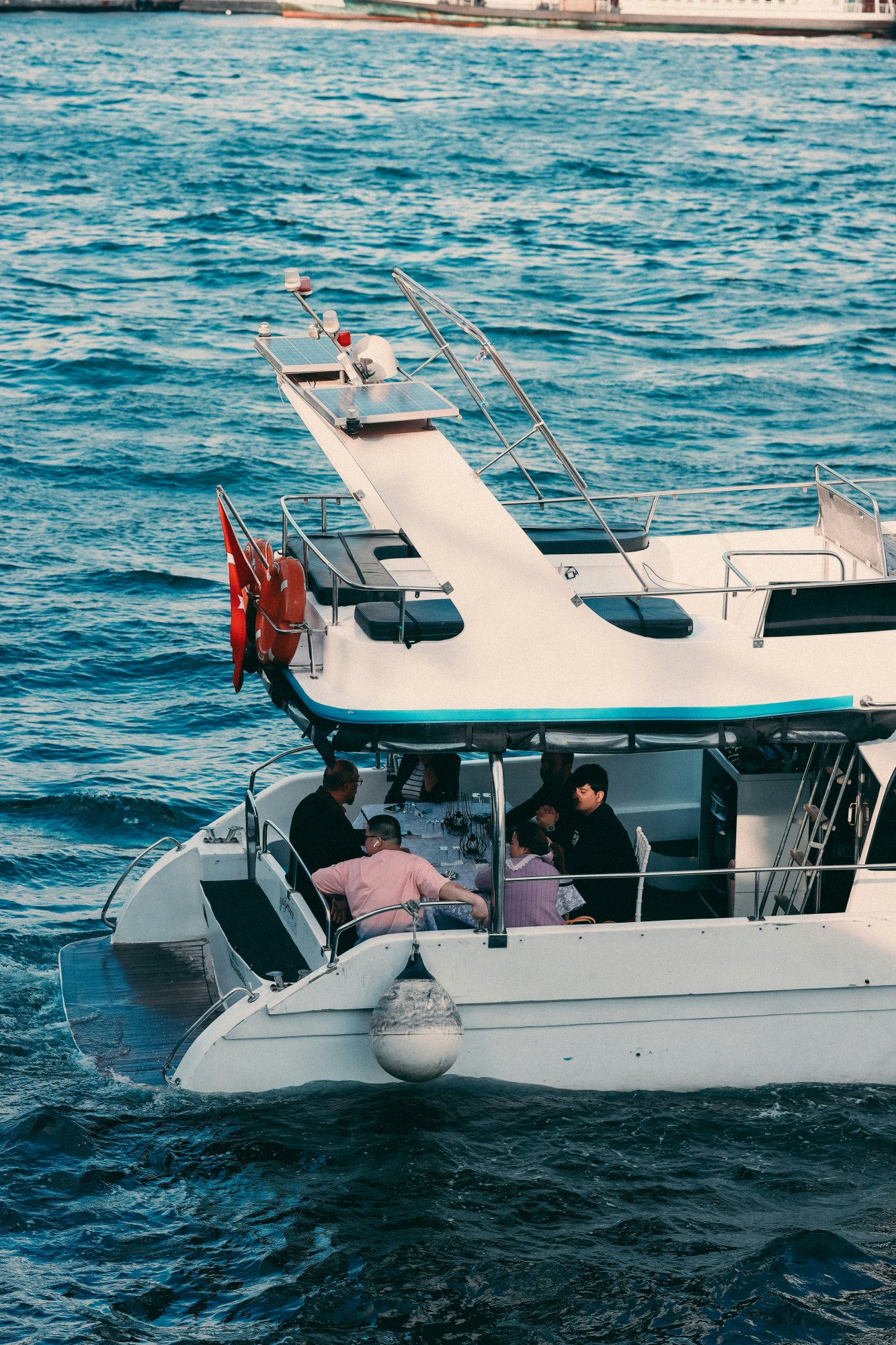 People dining on a boat with Turkish flag on a calm blue sea.